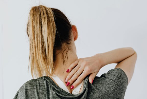 Back view of blond faceless lady in casual t shirt and manicure demonstrating pain spot on back while sitting near white wall